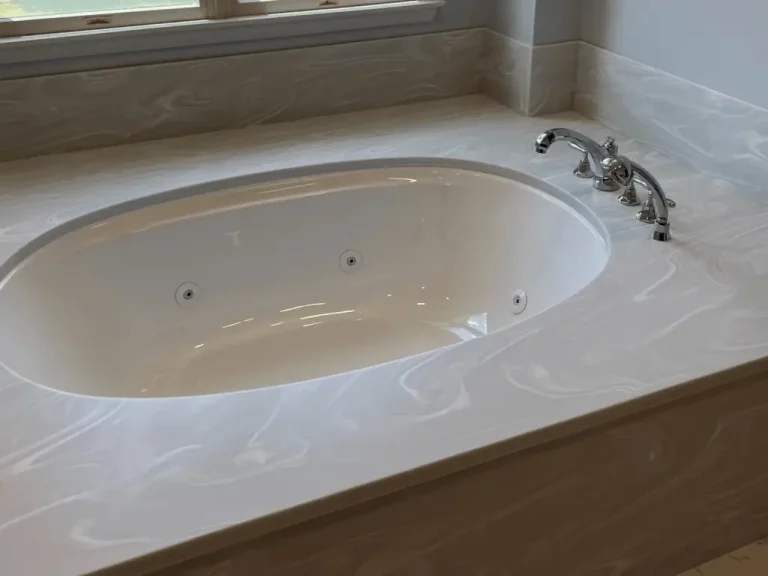 White solid surface whirlpool tub deck with a swirled marble pattern and chrome fixtures.