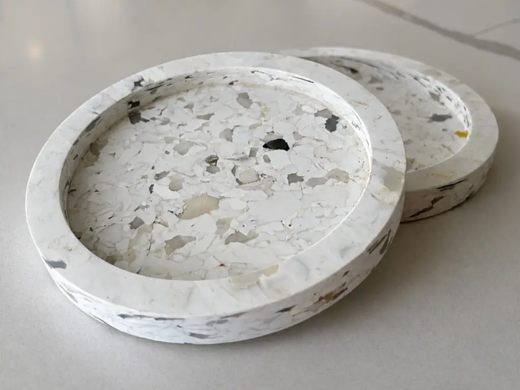 Two round Polygood recycled solid surface coasters with terrazzo-style fleck pattern.