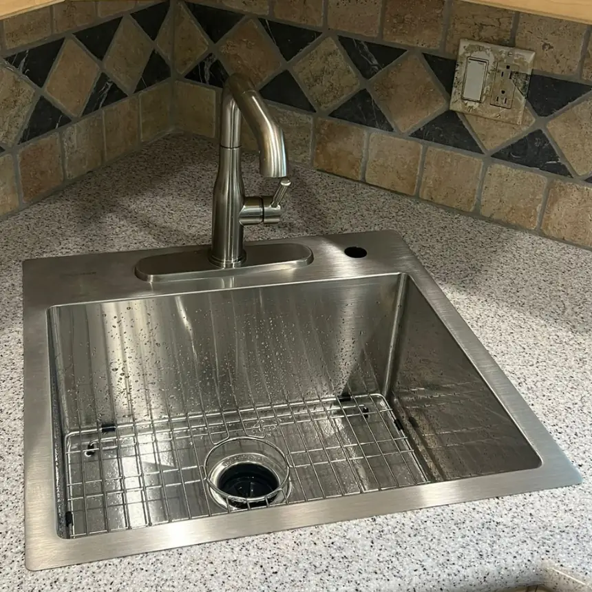 New stainless steel sink installed in a granite kitchen countertop after replacement.