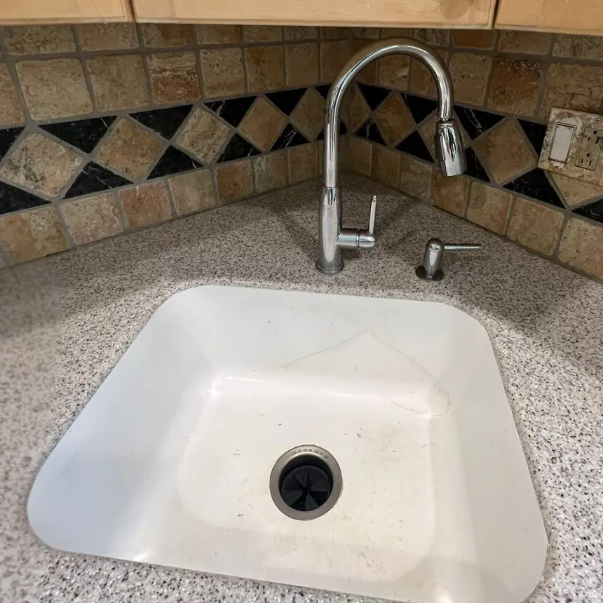 Worn white undermount sink in a solid surface kitchen countertop before replacement